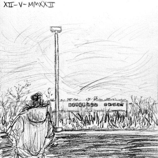 Jack stares out past a lamppost in a parking lot out to the woods and buildings ahead and up to the windy sky.